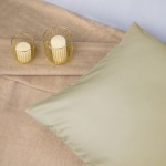 Poszewka satynowa 40x40 w kolorze kremowym leży na jasnym, miękkim tle. Produkt ma gładką, błyszczącą fakturę. Obok widoczne są dwa świeczniki z okrągłymi, kremowymi świecami. Układ jest jasny i minimalistyczny.