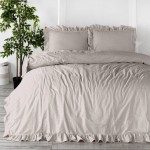 Komplet poszewek bawełnianych z falbanką 2x40x40 cm w kolorze kremowym, leżący na łóżku. Widoczna struktura materiału oraz falbanka przy krawędzi. Tło z drewnianą podłogą i rośliną doniczkową w tle.