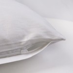 Poszewka satynowa 50x70 w kolorze białym, leżąca na gładkiej białej powierzchni. Widoczny zamek błyskawiczny w dolnej części poszewki. Gładka, błyszcząca faktura materiału, która odzwierciedla światło.