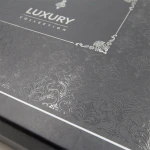 Opakowanie pościeli w kolorze ciemnoszarym z tłoczeniem w stylu żakardowym. Na wieczku widoczny napis LUXURY COLLECTION w eleganckim, srebrzystym kolorze. Kąt ujęcia z góry, pokazujący szczegóły wzoru.
