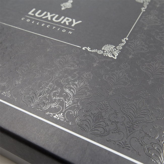 Zbliżenie na eleganckie, czarne opakowanie z wyraźnym, połyskującym wzorem żakardowym w odcieniach srebra. Na górnej części widoczny napis LUXURY COLLECTION. Opakowanie jest zamknięte, z dekoracyjnymi detalami na rogach.