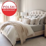 Prześcieradło jersey z elastanem w kolorze białym, rozmiar 180x200, leżące na łóżku z jasną pościelą. Widoczna tekstura materiału, która zapewnia elastyczność. W tle elementy wystroju sypialni, takie jak połyskująca lampa i dekoracyjne poduszki.