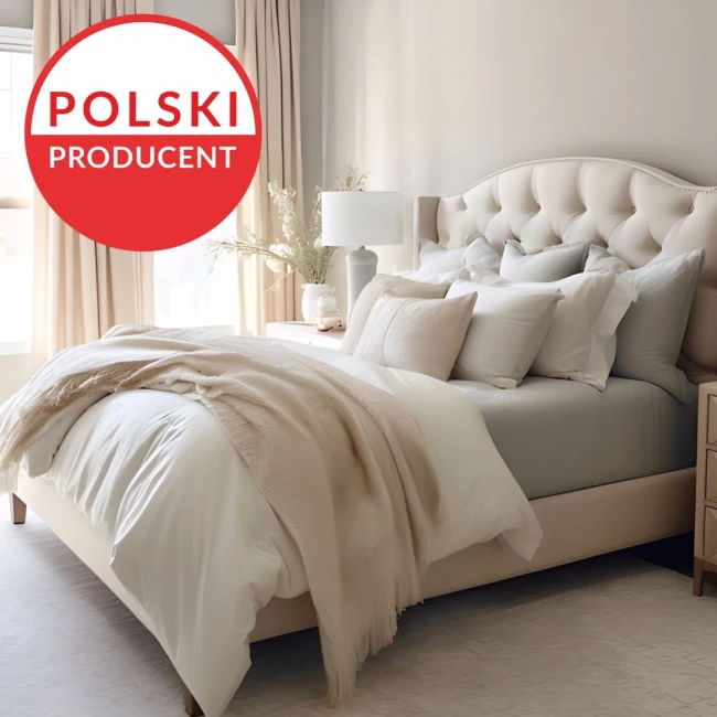 Prześcieradło jersey z elastanem, w kolorze beżowym, leży rozłożone na łóżku. Wymiary 200x220 cm. Na zdjęciu widoczne jest również kilka poduszek w różnych odcieniach beżu i szarości oraz jasna narzuta. Tło stanowi uporządkowane wnętrze sypialni.