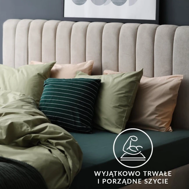 Prześcieradło jersey z gumką w kolorze antracytowym rozłożone na łóżku, z widoczną fakturą materiału. W tle poduszki w odcieniach zieleni i beżu. Kąt ujęcia z boku, prezentujący detale i układ elementów w sypialni.