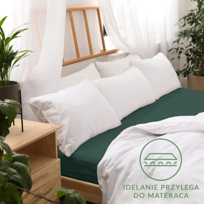 Zielone prześcieradło jersey z gumką, rozmiar 90x200, leży na łóżku, idealnie przylegając do materaca. W tle widoczne białe poduszki oraz minimalistyczne drewniane meble. Na zdjęciu widoczne logo z napisem Idealnie przylega do materaca.