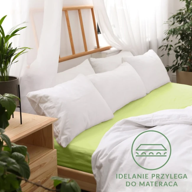 Prześcieradło jersey z gumką 180x200 w kolorze limonkowym leży na łóżku z białymi poduszkami. Widoczne są jego gładka faktura i elastyczne krawędzie. Tło zawiera drewniane elementy oraz roślinność, co tworzy przytulny klimat.