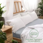 Prześcieradło jersey z gumką 200x220 w kolorze popiel, rozłożone na łóżku z białymi poduszkami. Widoczna gładka faktura materiału, który idealnie przylega do materaca. Tło z naturalnymi dekoracjami i drewnianą ramą łóżka.