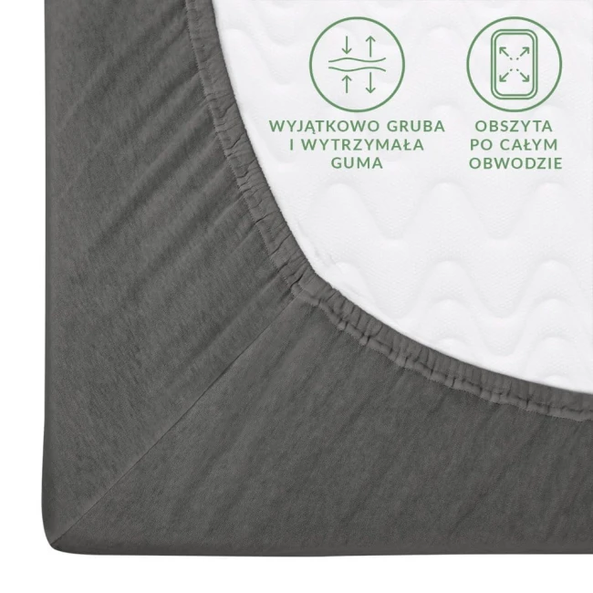 Prześcieradło jersey z gumką 140x200 w kolorze szarym, pokazane w zbliżeniu na róg, z widoczną teksturą materiału. Gruba gumka obwodowa zapewnia optymalne dopasowanie. Na białym tle wyraźne napisy informacyjne na jasnym, falistym tle.