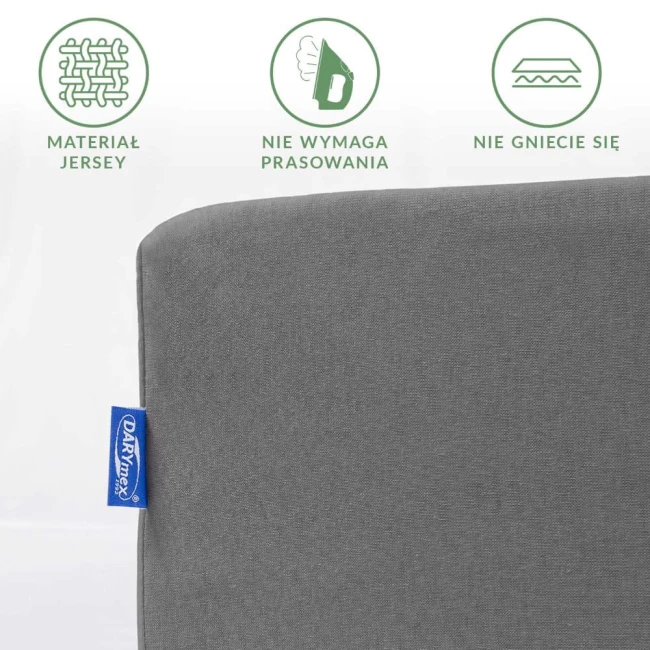 Prześcieradło jersey z gumką 200x220 w kolorze szarym, z widocznym logo, złożone w prostokąt. Tkanina nie wymaga prasowania i nie gniecie się, umieszczone na jasnym tle. Tekstura materiału miękka i gładka.