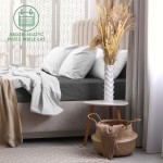 Prześcieradło frotte z gumką 180x200 w kolorze antracytowym, rozłożone na materacu, z poduszkami i narzutą w jasnych odcieniach. W tle stół z wazonem i dekoracjami, na jasnym tle, tworzącym przytulną aranżację sypialni.