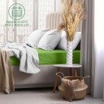 Prześcieradło frotte z gumką w kolorze kaktus leży na łóżku, z widoczną białą pościelą. Produkt rozciąga się na materacu 160x200, z widoczną gumką brzegową. W tle widać stylową poduszkę i kwiaty w wazonie na stoliku. Tło jest jasne i zdobione.