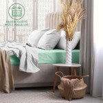 Prześcieradło frotte z gumką w kolorze morskim o wymiarach 200x220 cm, rozłożone na łóżku z szarymi poduszkami. W tle widoczny stół nocny z wazonem i dekoracyjnymi trawami oraz koszem.