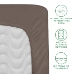 Prześcieradło satynowe z gumką 140x200 w kolorze sepia. Widoczny detal gumy obszytującej po całym obwodzie, zapewniający stabilne dopasowanie. Produkt leży na materiale w fakturze białej, z delikatnym wzorem. Kąt ujęcia: z boku.
