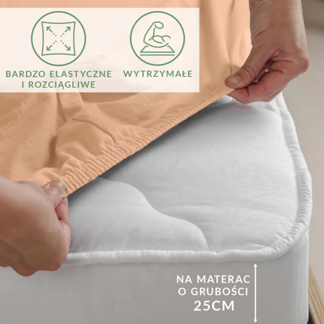 Prześcieradło jersey z elastanem w kolorze różowym, rozłożone na białym materacu o grubości 25 cm, z widoczną elastyczną gumką. W tle niejednolita powierzchnia. Na materiale znajduje się informacja o trwałości i elastyczności.