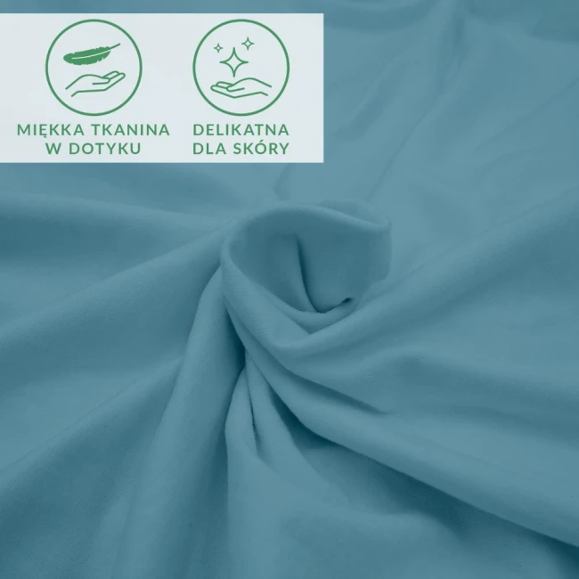 Prześcieradło jersey z elastanem 200x220 w kolorze błękitnym, leżące na płasko z wyraźną fakturą materiału. W tle widoczne ikony informacyjne: miękka tkanina w dotyku oraz delikatna dla skóry.