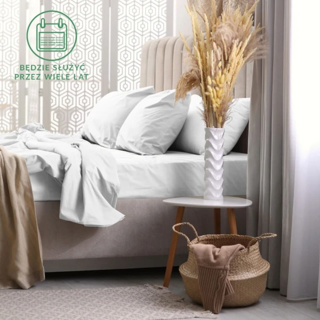Prześcieradło frotte z gumką o wymiarach 70x140 cm w kolorze białym, rozłożone na łóżku, z widocznymi poduszkami. W tle delikatne dodatki, jak wazon z suszonymi kwiatami na stoliku. Tło neutralne, jasne.