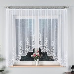 Firana gotowa Berenika żakardowa biała, o wymiarach 300x160 cm, z subtelnym wzorem w dolnej części. Zawieszona na karniszu, widoczne przezroczystości. Otoczenie: jasna ściana i kwiatek w doniczce na parapecie.