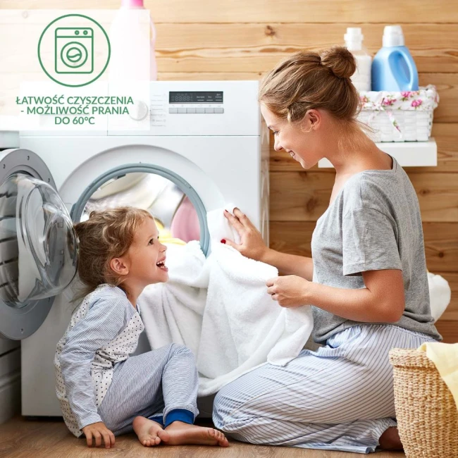 Matowa biała pralka z okrągłym otworem, w której widać ręcznik. Matka w szarej bluzie i dziecko w piżamie siedzą obok, śmiejąc się. Tło z drewnianymi panelami i kosmetykami do prania. W widoku plakat z informacją o łatwości czyszczenia do 60°C.