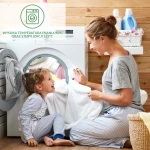 Ochraniacz na materac 90x200, biały, rozłożony na podłożu, z widocznościami na teksturę materiału. Ujęcie frontalne, na wprost, ze szczegółami haftu lub zszywek. W tle pralka oraz kosz na bieliznę, co sugeruje kontekst prania.