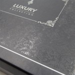 Czarna, matowa pudełko z delikatnym, tłoczonym wzorem w stylu barokowym oraz napisem LUXURY COLLECTION. Ujęcie z góry, zbliżenie na detale wzoru. Idealne do przechowywania pościeli.
