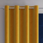 Welwetowa zasłona w kolorze szafranowym, rozmiar 140x260 cm, z przelotkami. Powieszona na karniszu, ukazuje gładką, miękką fakturę tkaniny, ustawiona w pionie. Tło w ciemnym kolorze, co podkreśla intensywność żółtego odcienia.