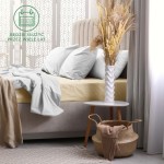 Prześcieradło frotte z gumką 200x220 w kolorze jasnego beżu, leżące na łóżku, z poduszkami w jasnym odcieniu. W tle nowoczesna aranżacja z wazonem oraz koszem. Widoczna faktura materiału, prezentująca się na minimalistycznym tle.
