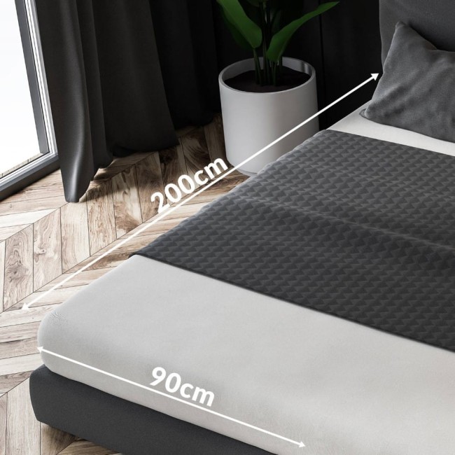 Prześcieradło frotte z gumką w kolorze zielenie butelkowej, rozmiar 90x200 cm, leżące na materacu. Widoczne wymiary, faktura materiału z wypukłym wzorem. Tło w aranżacji sypialni z rośliną i oknem, drewniana podłoga.