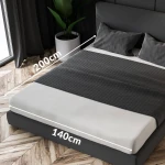 Prześcieradło frotte z gumką w kolorze zieleni butelkowej o wymiarach 140x200 cm, rozłożone na materacu. Widoczna faktura tkaniny oraz gumka mocująca. W tle widoczna roślina w donicy oraz część łóżka z pościelą w odcieniach szarości.