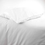 Poszewka na poduszkę 70x80 cm hotelowa, w białym kolorze z delikatnym paskiem 4 mm, leży na podłożu. Produkt jest złożony, a jego faktura jest gładka. Tło jest jasne i jednolite, co podkreśla prostotę designu.