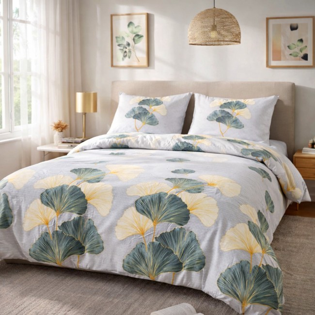 Pościel flanelowa 140x200 Solenne Light w odcieniach szarości z grafiką liści miłorzębu w kolorach zielonym, białym i żółtym. Rozłożona na łóżku, widok frontalny. W zestawie poszwy na poduszki. Tło jasne, z lampą stołową w pobliżu.