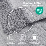 Koc bawełniany 200x220 w odcieniu szarym, leżący na płaskiej powierzchni, z frędzlami na krótszym boku. Widać teksturę materiału, który jest delikatny i miękki, idealny do użytku domowego lub dopełnienia aranżacji wnętrz.
