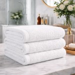 Biały ręcznik hotelowy 70x140 cm, gładki, o gramaturze 400 g/m², ułożony w stosie na marmurowym blacie, z widocznymi brzegami i teksturą materiału, w tle łazienka z roślinnością i dekoracjami.