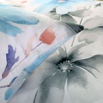 Pościel satyna bawełniana 180x200 w kolorze białym zdobiona dużymi pastelowymi niebieskimi kwiatami. W zestawie widoczne poduszki z delikatnym nadrukiem. Materiał gładki, z połyskiem, idealny do eleganckiej sypialni.