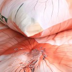 Pościel satyna bawełniana 140x200 Camellia w kolorze kremowym z pomarańczowymi kwiatami. Widoczne detaliczne wzory kwiatowe na poszewce i kołdrze, materiał gładki i błyszczący, leżące na łóżku w zbliżeniu.