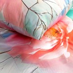 Pościel satyna bawełniana 160x200 w kolorze szarym i zielonym z różowymi kwiatami. Zbliżenie na poszewki z delikatnym wzorem, na tle materiału w pastelowych odcieniach, ukazującym detale kwiatów i gałązek.